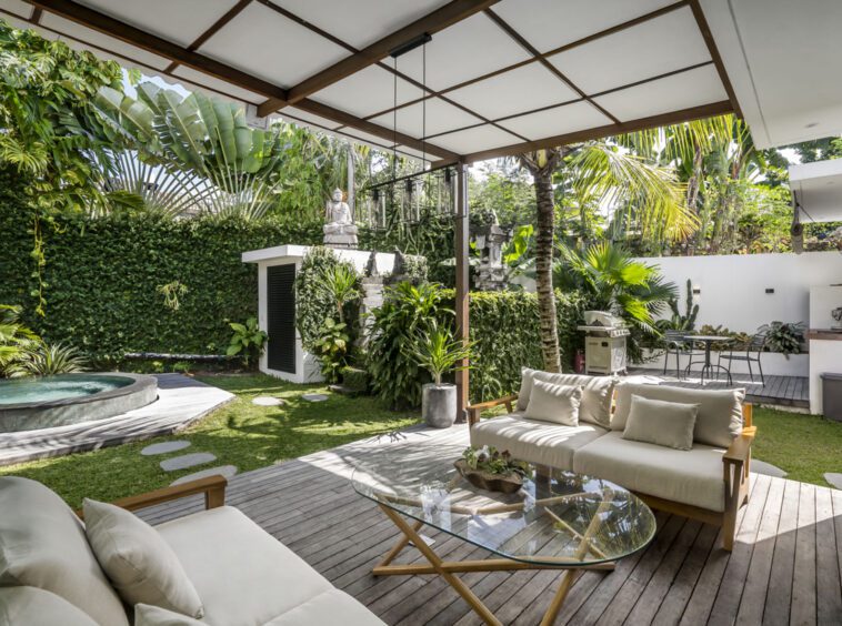 Outdoor lounge area with two couches that is surrounded by lush greenery. In the background, a jacuzzi can be spotted.