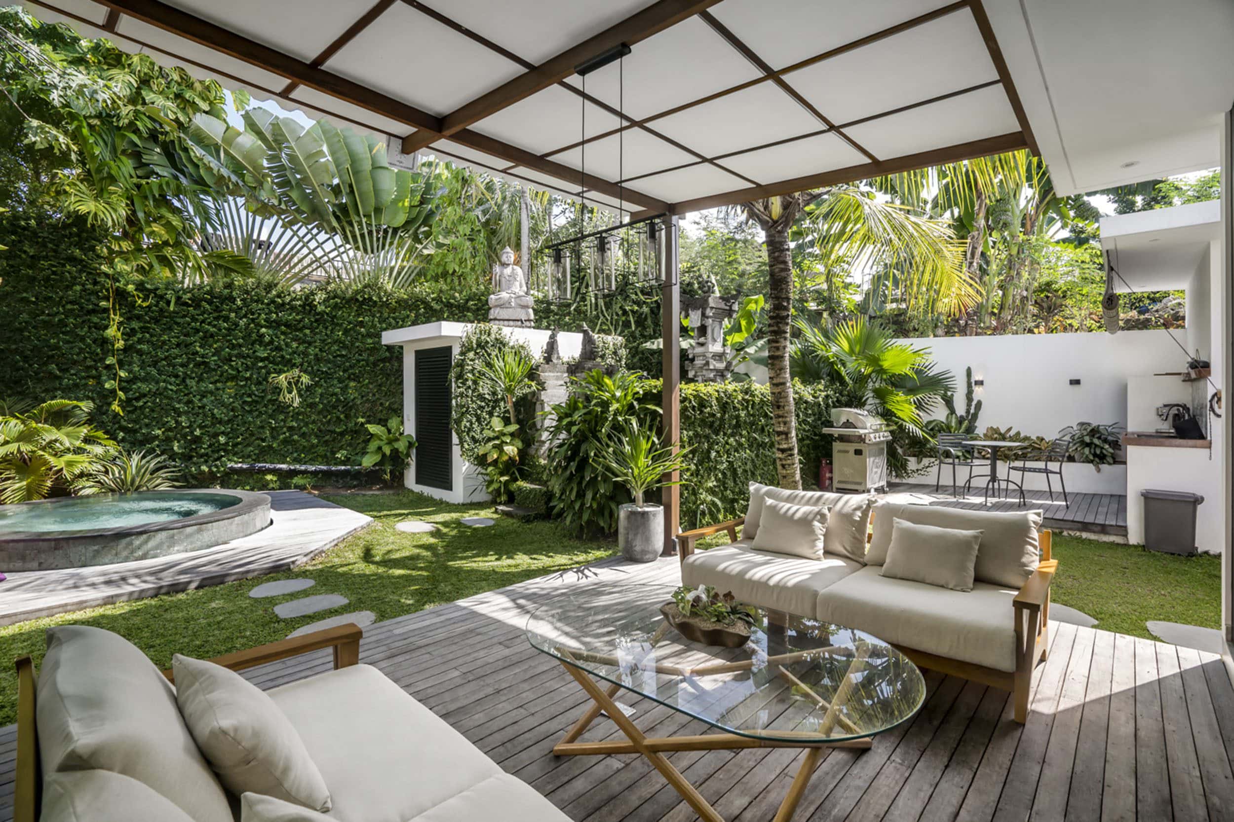 Outdoor lounge area with two couches that is surrounded by lush greenery. In the background, a jacuzzi can be spotted.