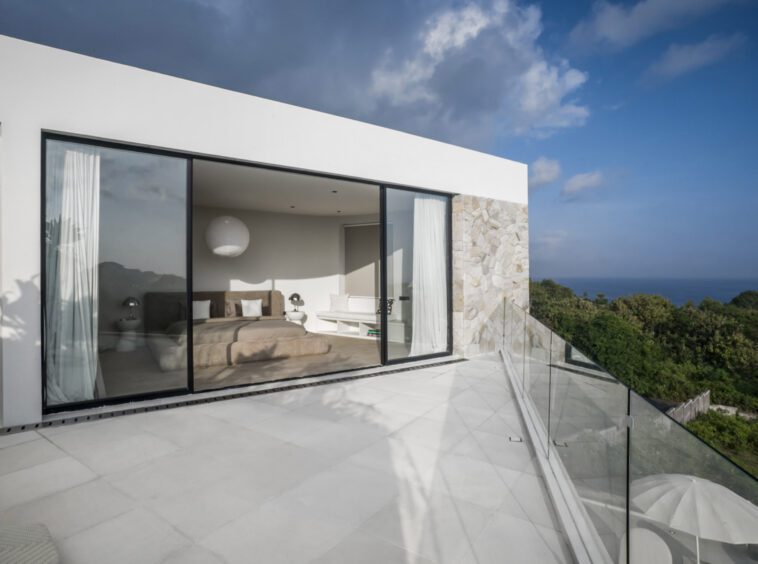 A private villa in Bingin with terrace doors open and looking into the bedroom. The terrace view is a green forest with ocean view in the horizon