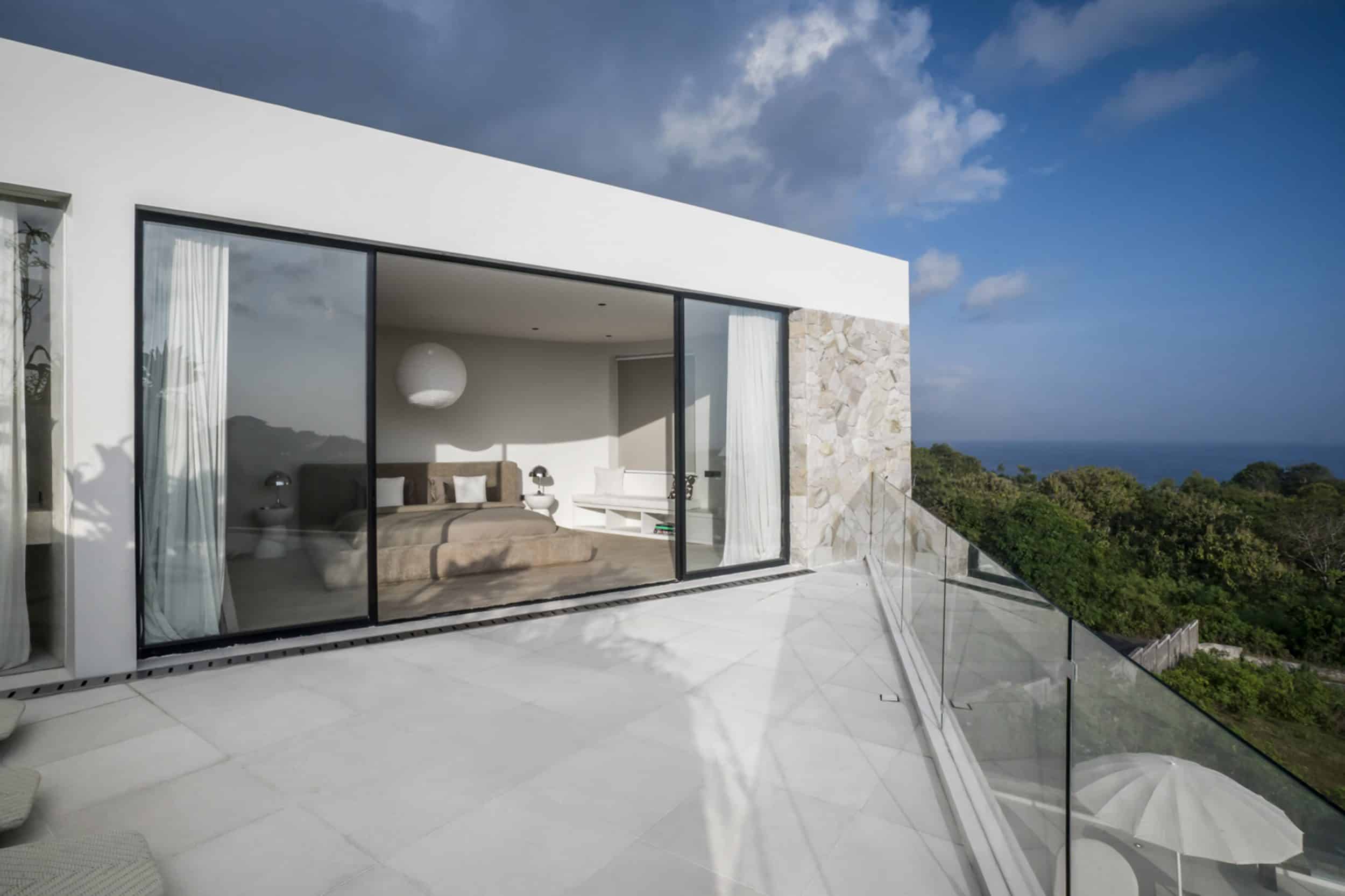 A private villa in Bingin with terrace doors open and looking into the bedroom. The terrace view is a green forest with ocean view in the horizon