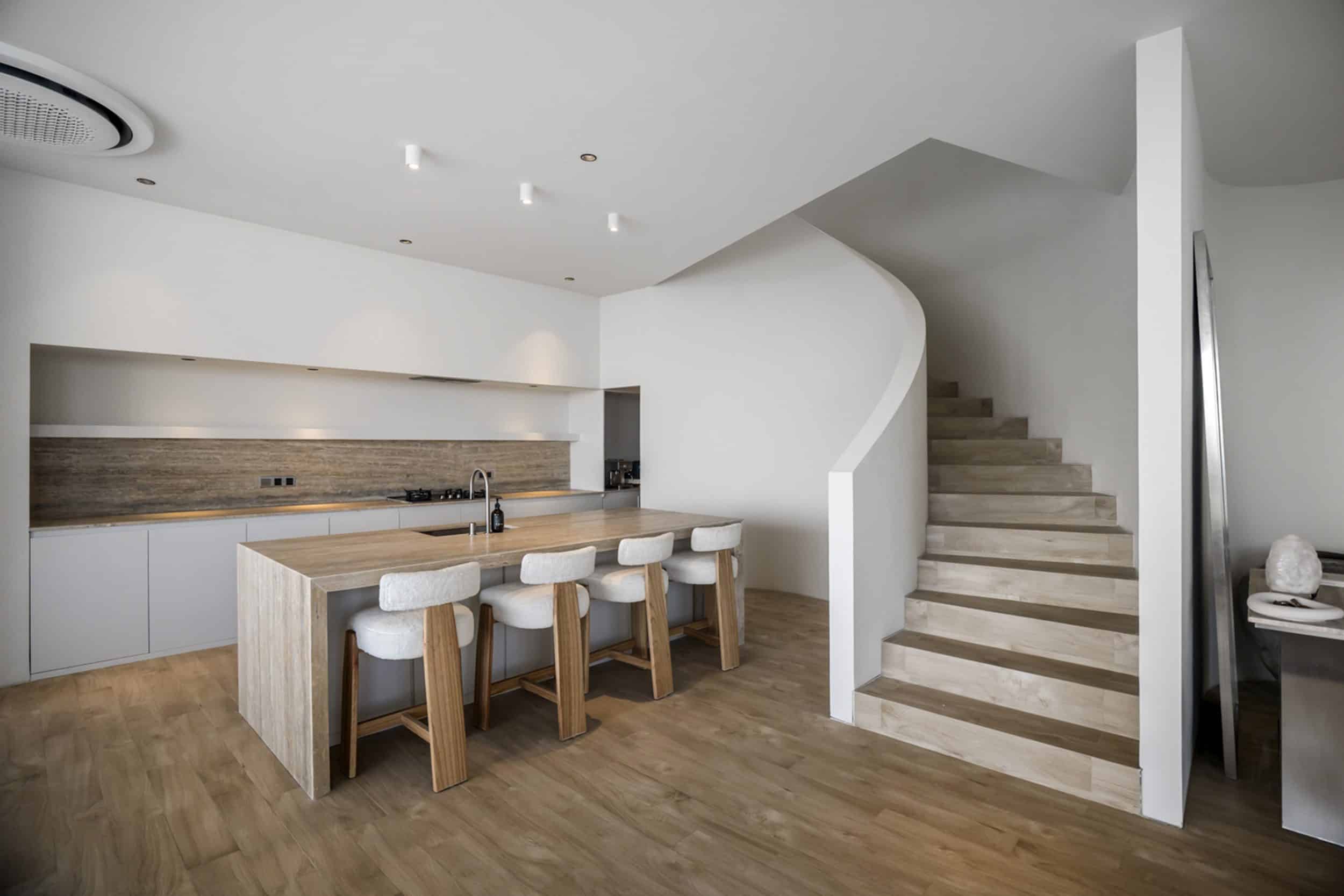 Kitchen area with a bar top and bar stools, situated next to some stairs going upstairs of this private villa in Bingin