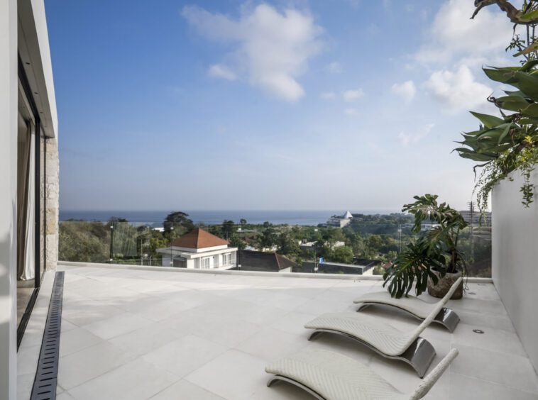 Terrace of a private villa in Bingin with three sun loungers and view of the neighbouring area with the ocean in the distance