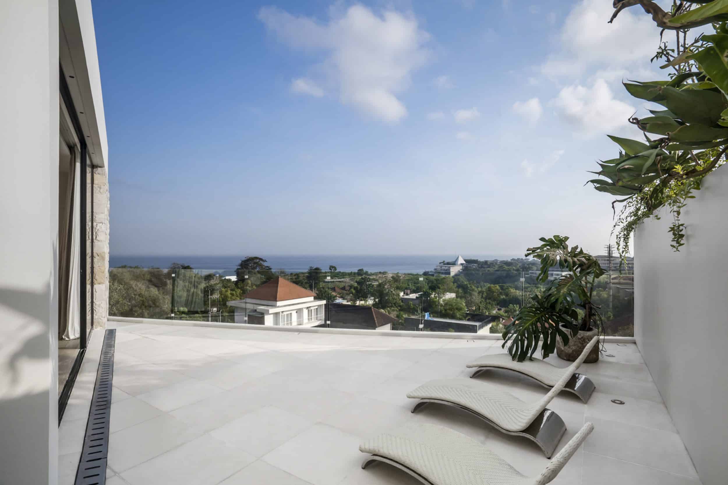 Terrace of a private villa in Bingin with three sun loungers and view of the neighbouring area with the ocean in the distance