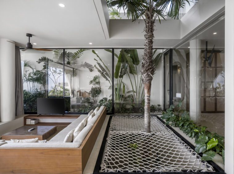 Living room of a tropical Uluwatu villa with a palm tree in the center next to a TV lounge area