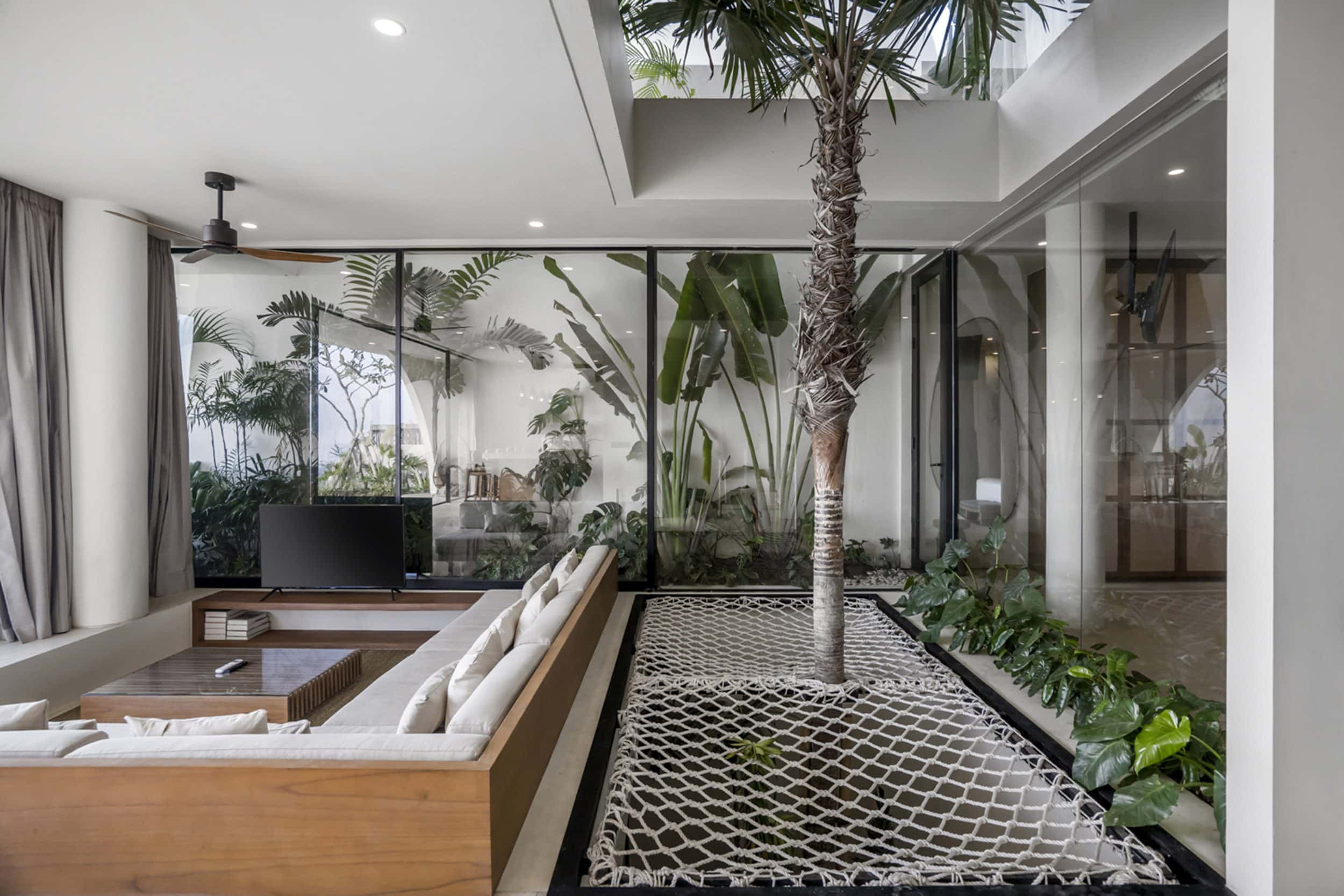 Living room of a tropical Uluwatu villa with a palm tree in the center next to a TV lounge area